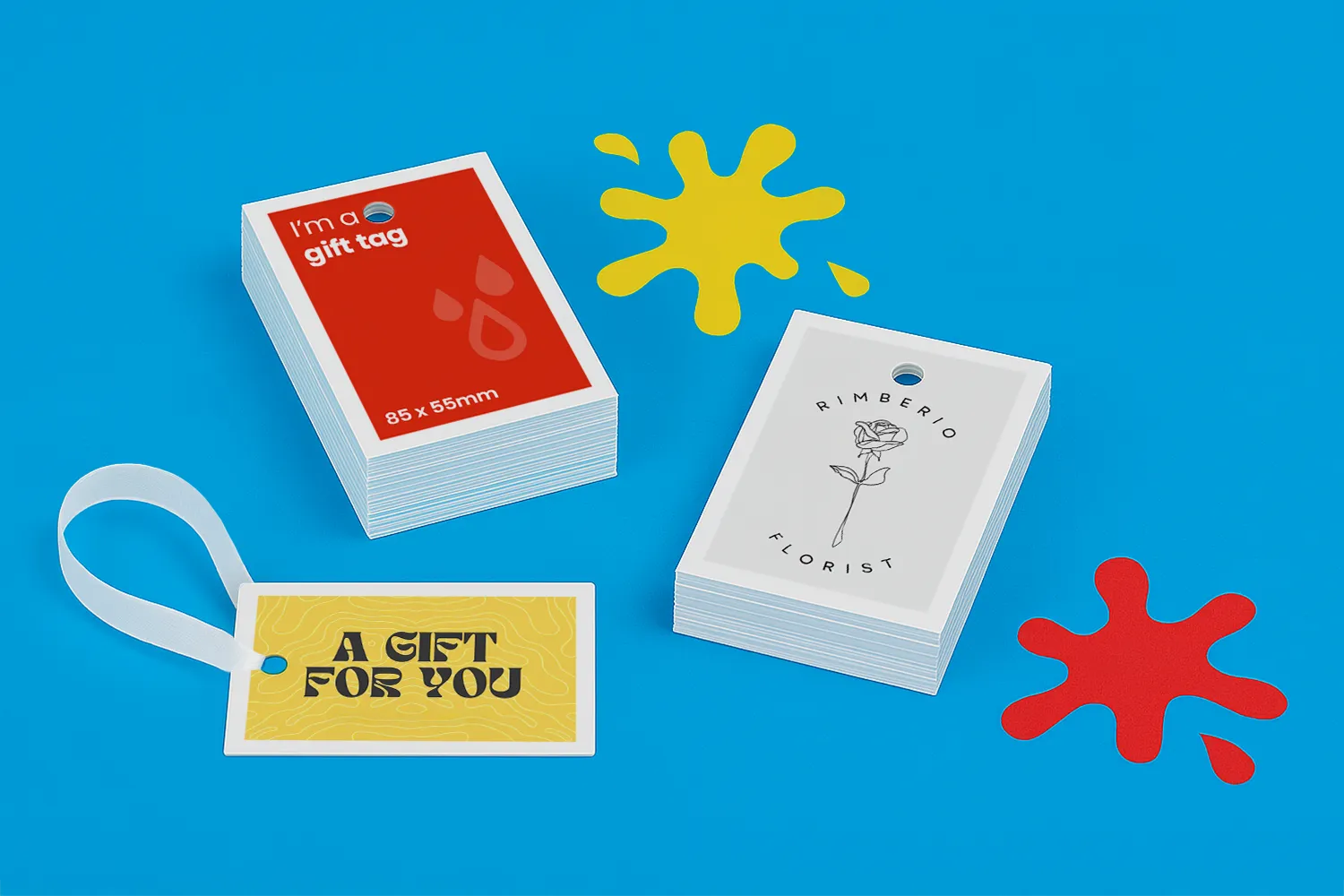 Three stacks of assorted gift tags on a blue surface with yellow and red paint splatters.