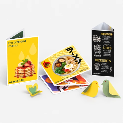 Three folded restaurant menus displayed with paper cutouts of a butterfly and two birds.