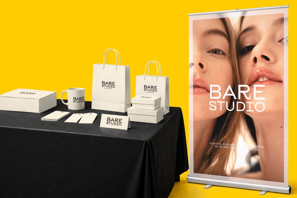 Table with BARE STUDIO branded items and a banner showing two women's faces on a yellow background.