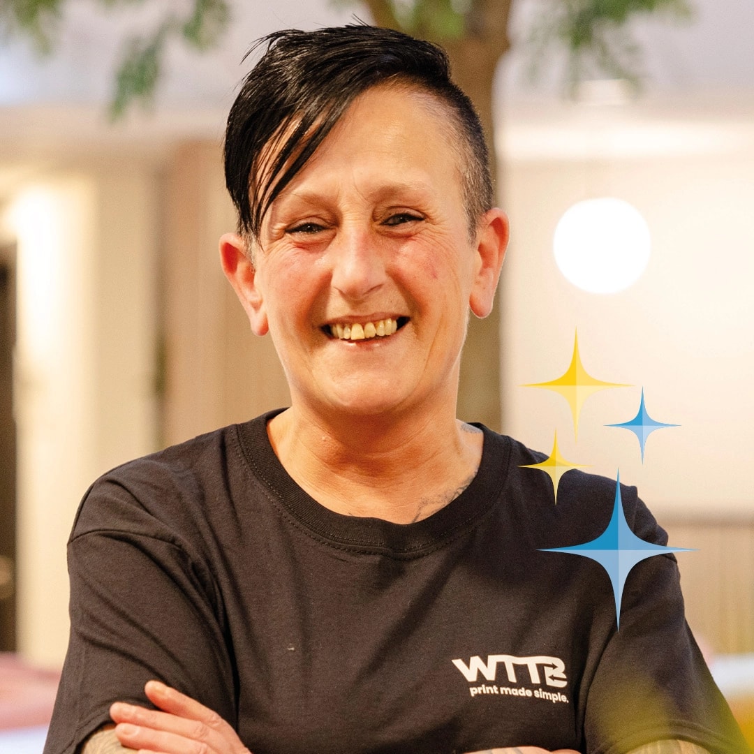 Person wearing a black shirt with "WTTB" logo, smiling with crossed arms.