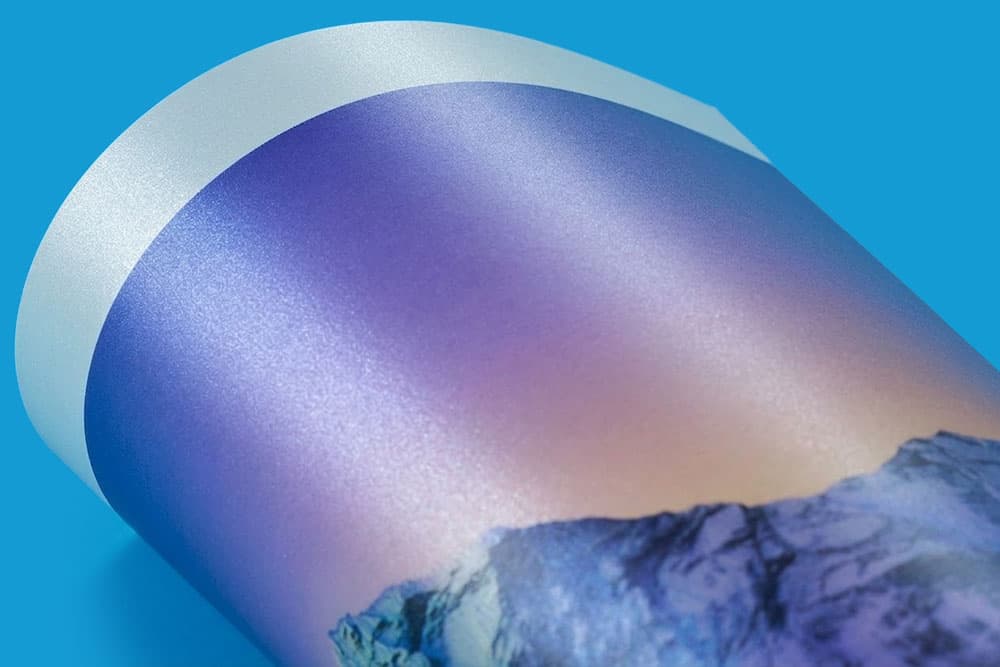 Close-up of a rolled, glossy print featuring a mountain landscape against a blue background.