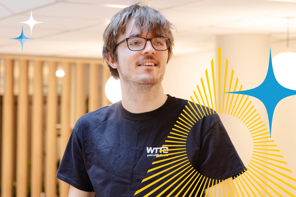 A person in glasses and a black WTTB t-shirt stands indoors with graphic shapes overlaid.