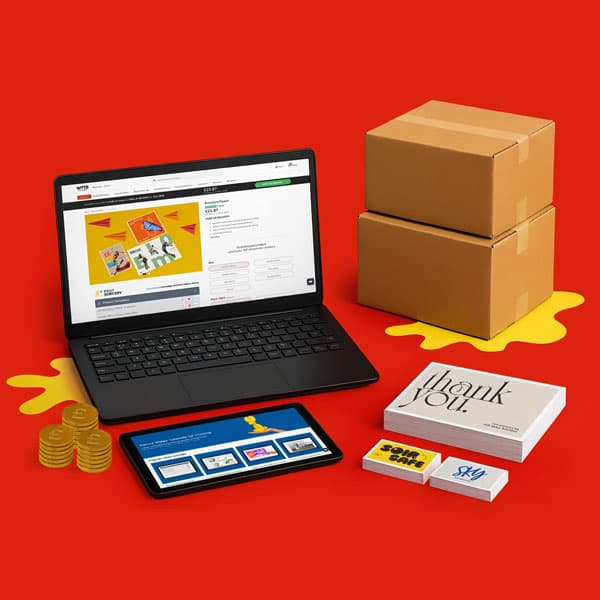Laptop, tablet, stacked boxes, coins, cards, and booklets on a red surface.