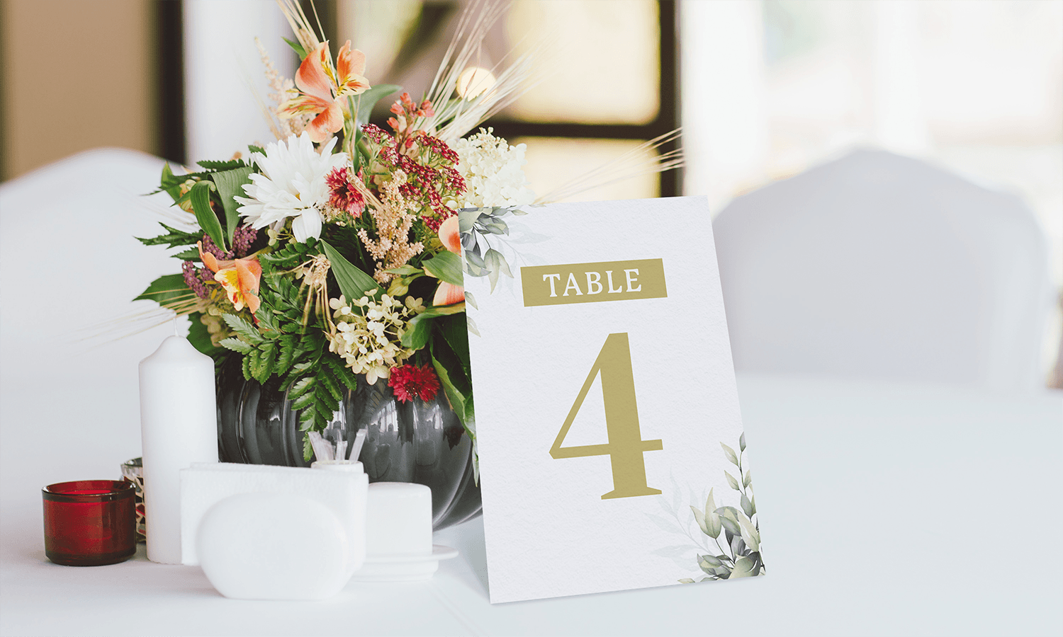 Wedding floral centrepiece and a custom table name card displaying "Table 4" on a white tablecloth in a wedding setting.