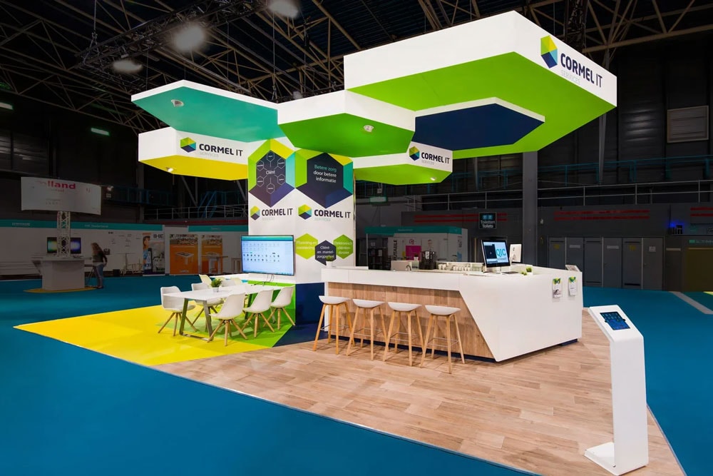 Modern trade show island stand with branding, seating areas, and digital displays.