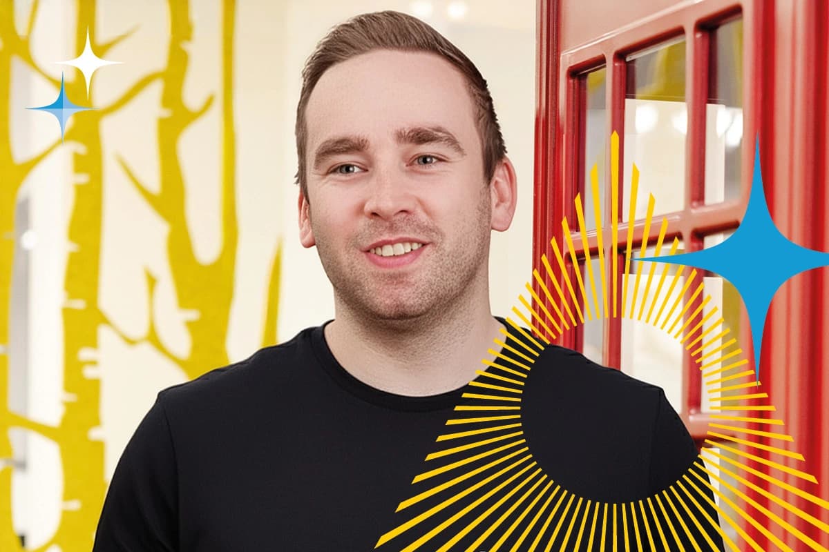 Man in a black shirt stands in front of a red booth and yellow wall with graphic overlays.