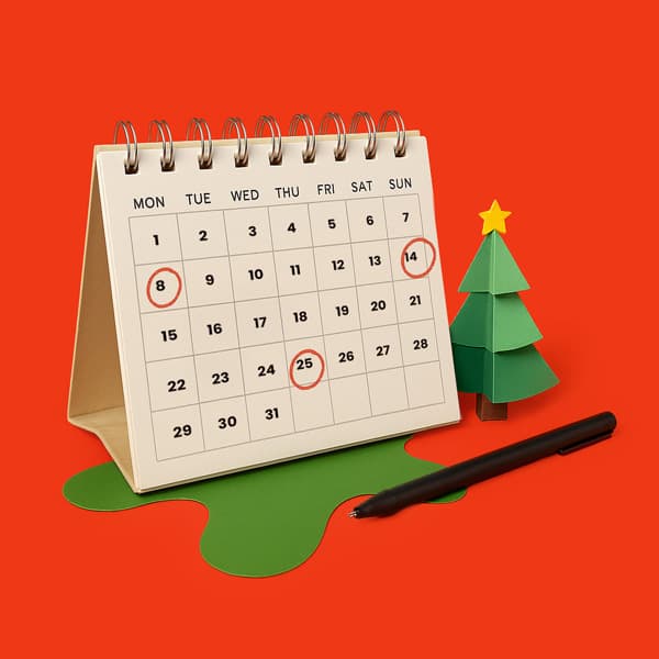 Desk calendar with December dates circled, a pen, and a paper Christmas tree on red background.