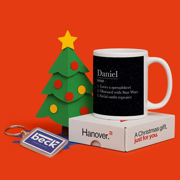 A mug, gift box, and keychain next to a paper Christmas tree on an orange background.