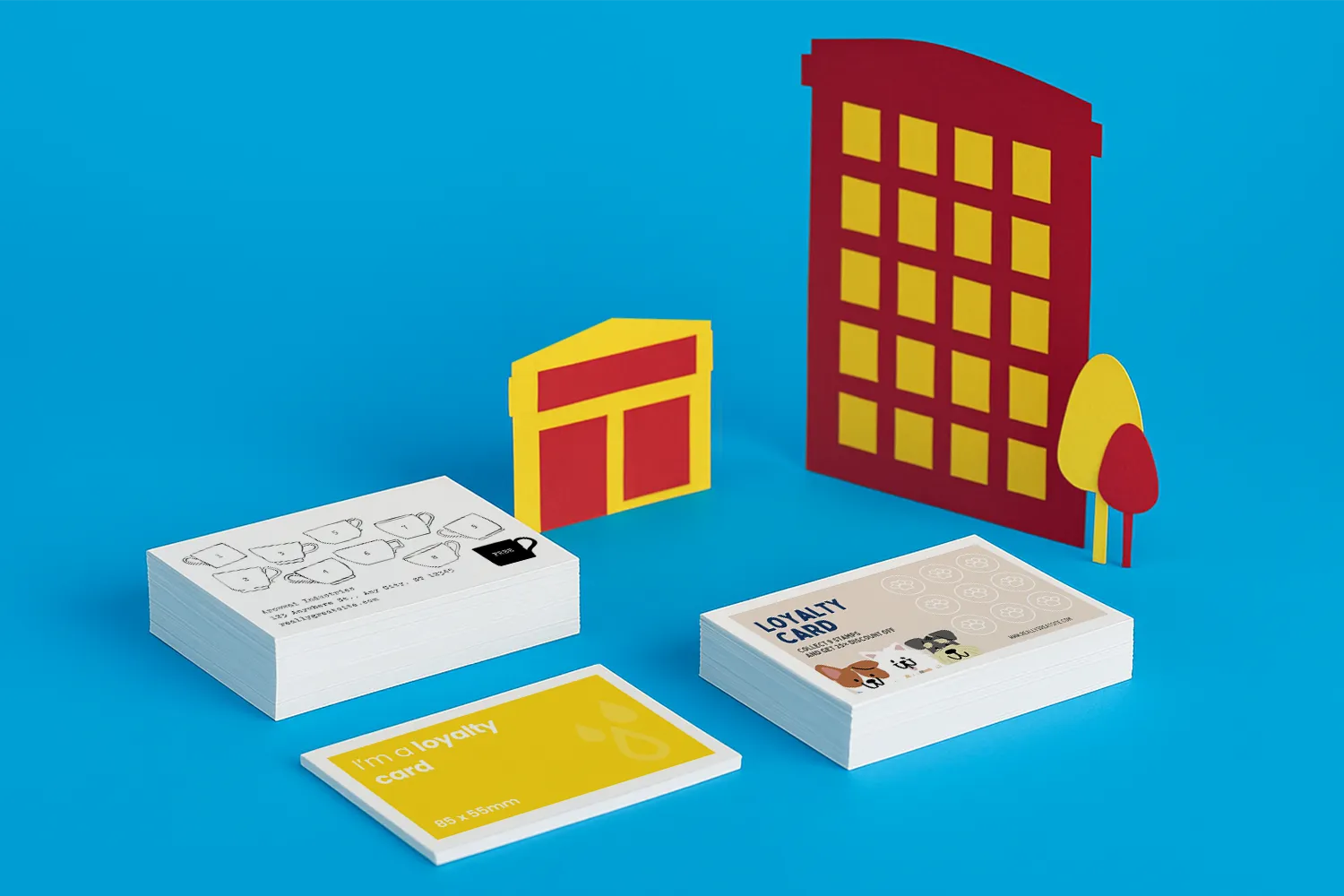 Stacks of loyalty cards are displayed on a blue surface with paper building and tree cutouts.