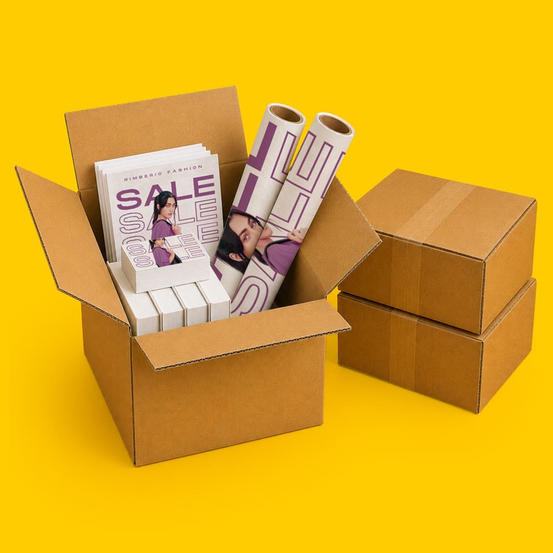Open cardboard box with books inside next to two closed boxes on a yellow background.