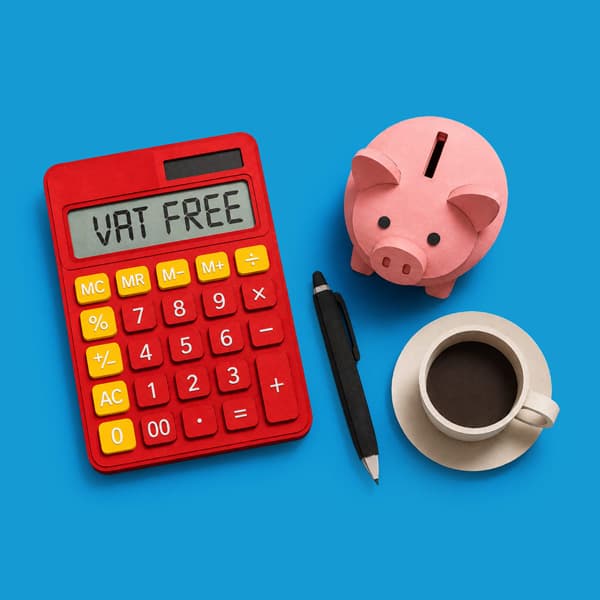 Red calculator with “VAT FREE” on display, pink piggy bank, pen, and coffee cup on blue background.