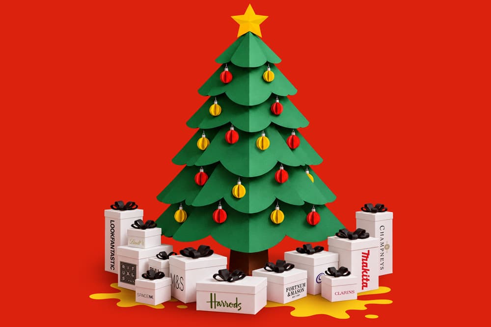 Paper Christmas tree with ornaments surrounded by branded gift boxes on a red background.