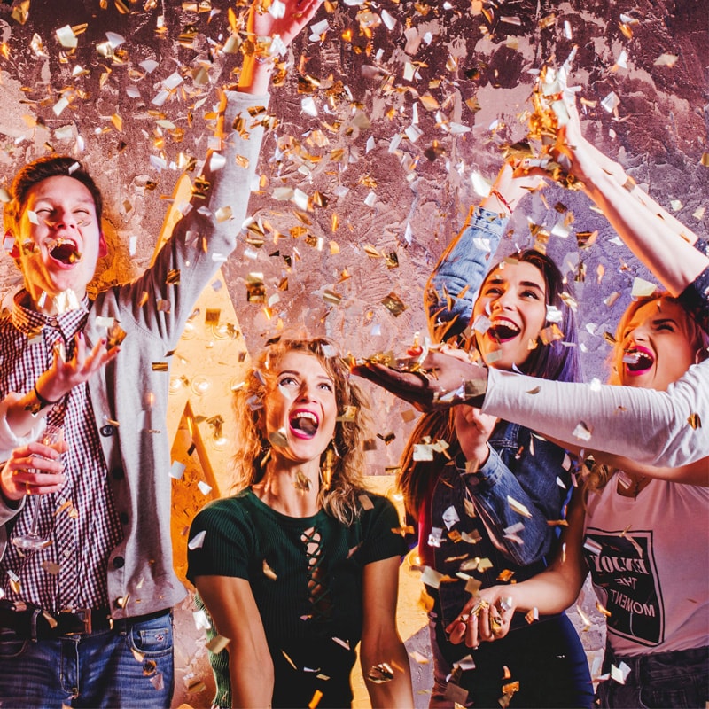 A group of people celebrate indoors, tossing confetti and smiling with excitement.