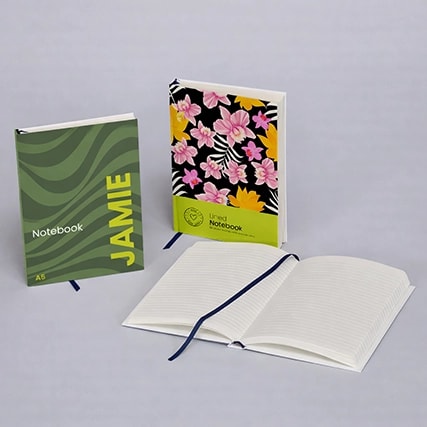 Three notebooks: one green with "JAMIE," one floral, and one open displaying lined pages.