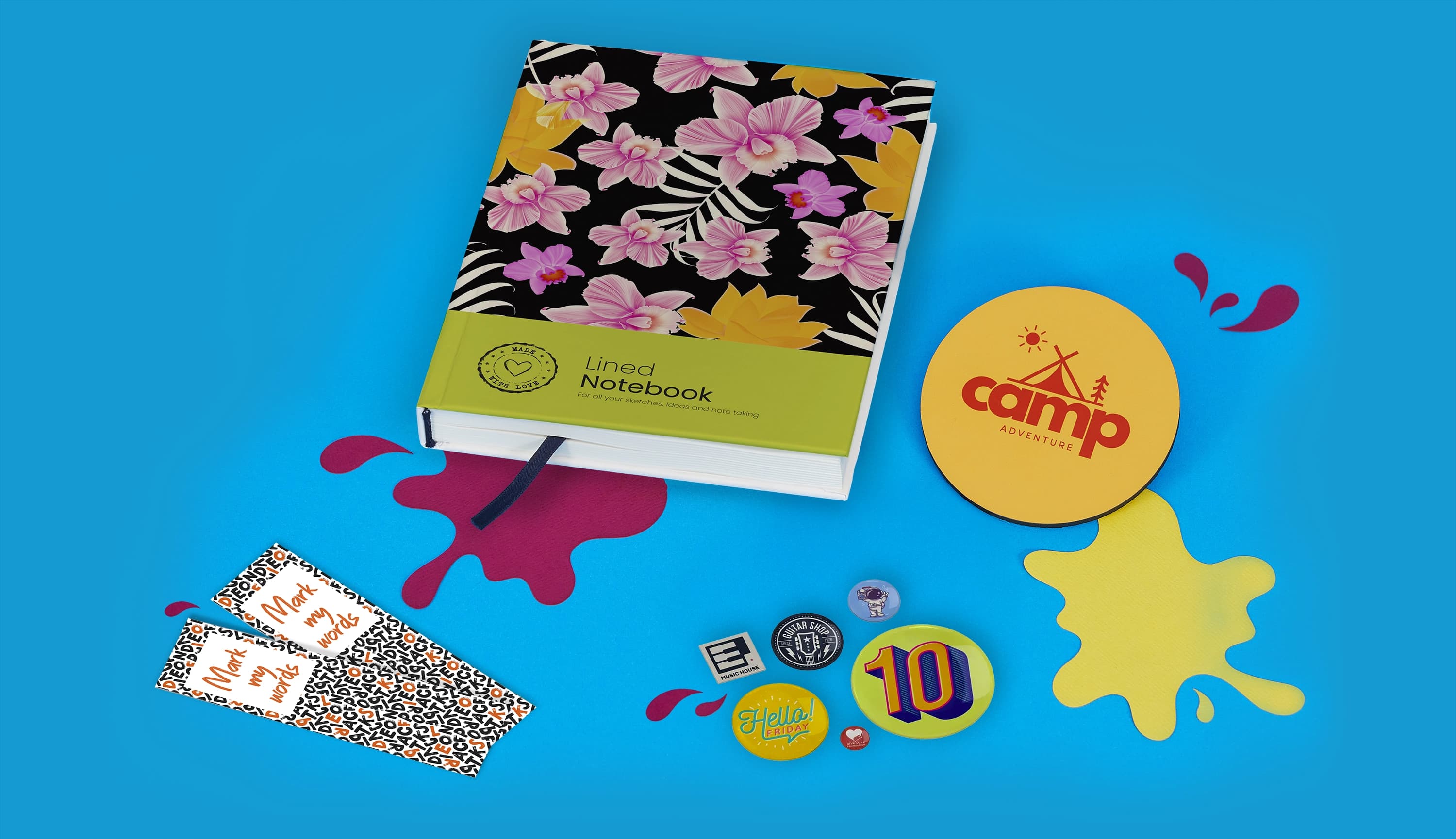 Notebook with floral cover, bookmarks, and assorted pins on a blue background.