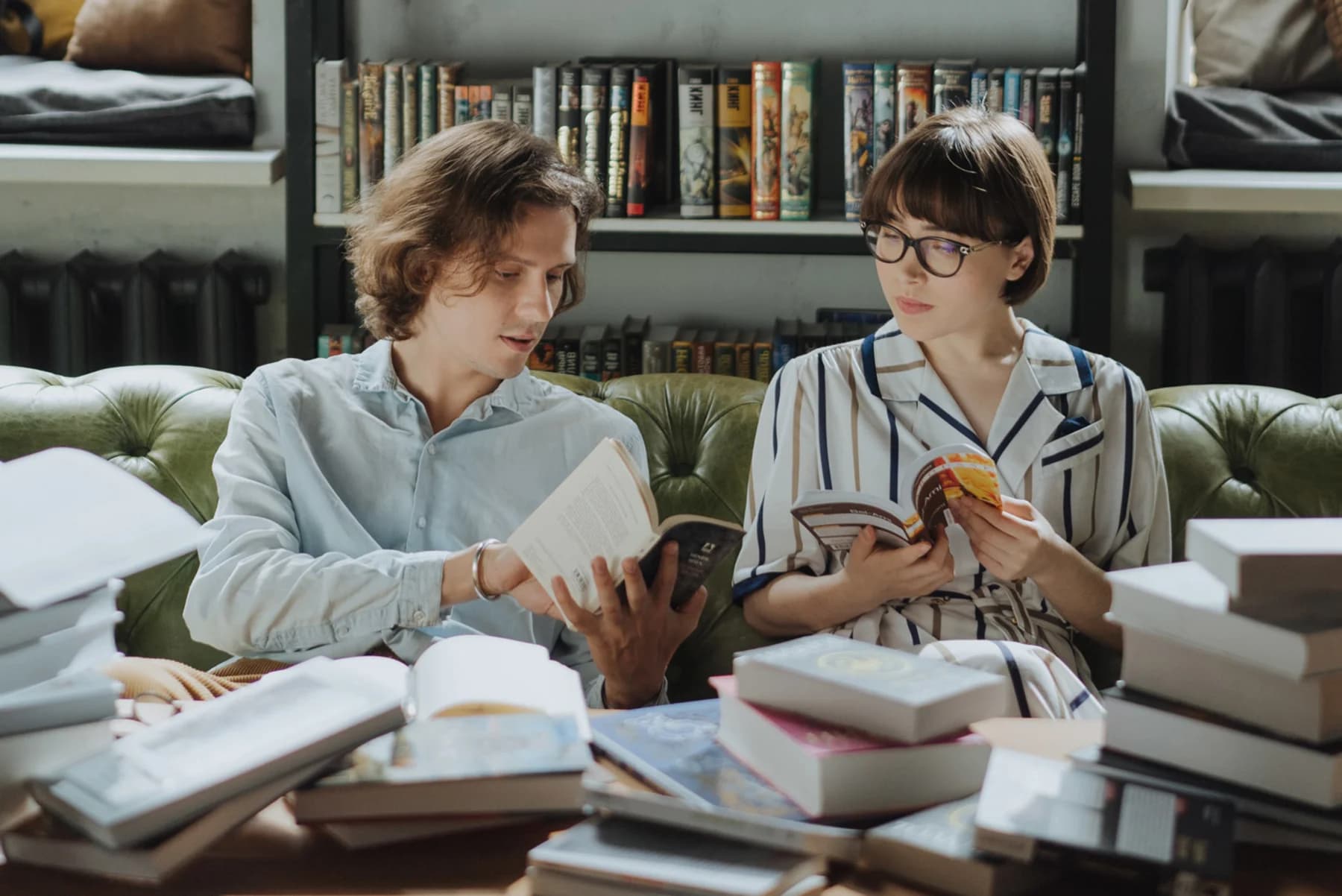 Two individuals seated on a couch, surrounded by books and a laptop, engaged in a study session together