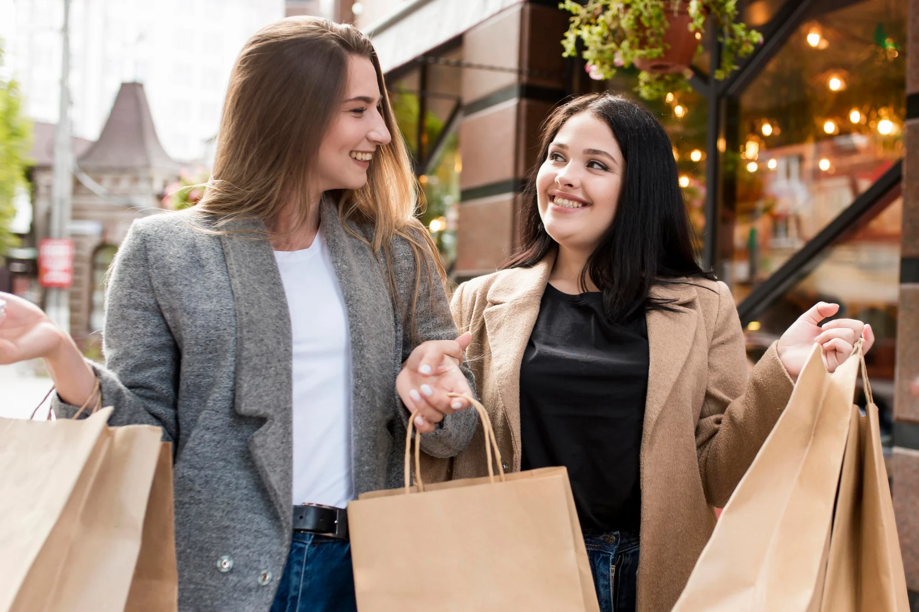Two women joyfully smiling while holding colourful shopping bags in their hands