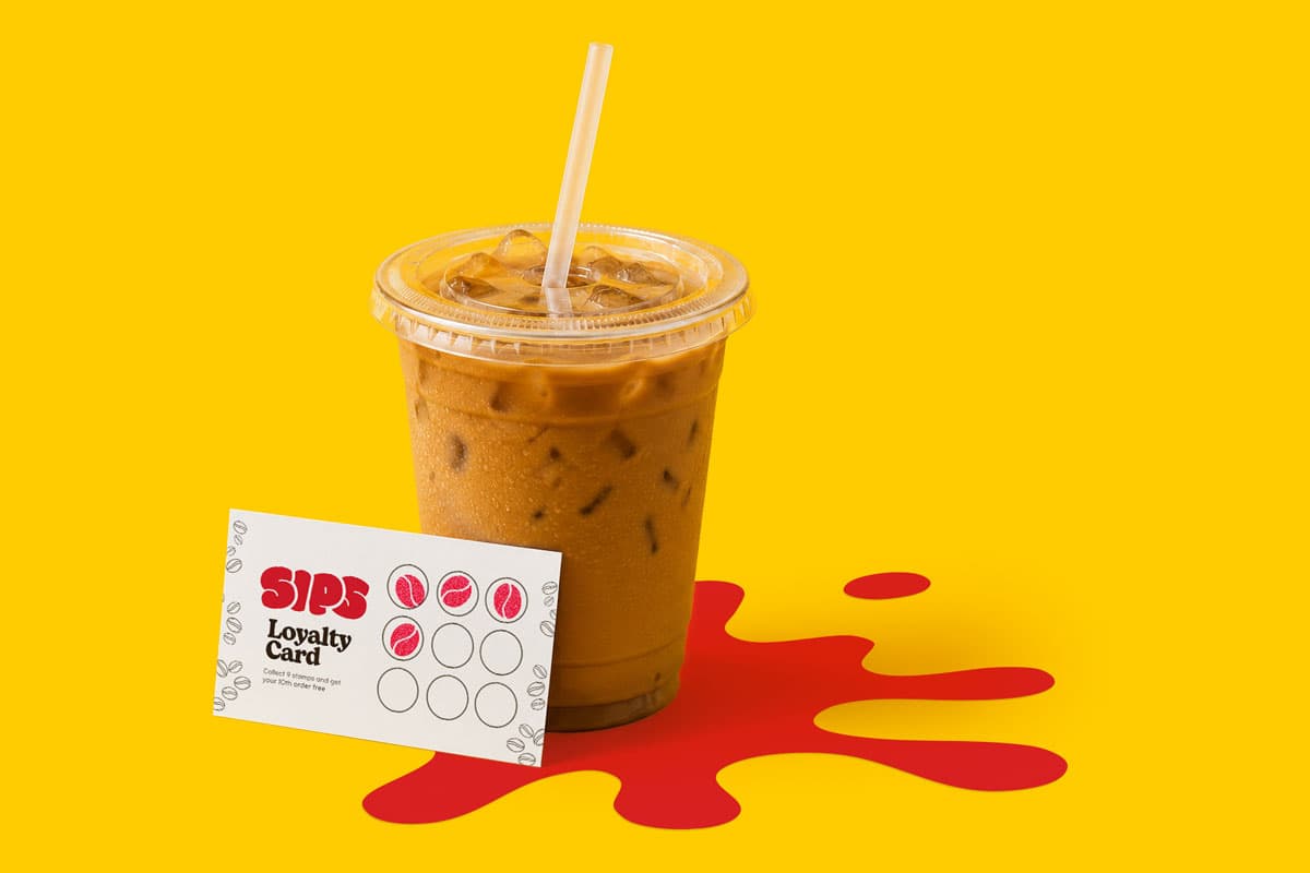 Iced coffee in plastic cup with straw next to a SIPS loyalty card on a yellow background.