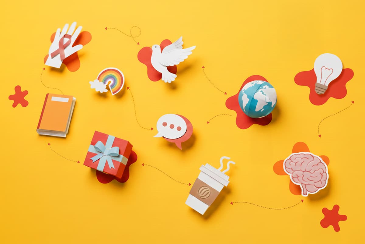Paper cutout icons of a ribbon, dove, book, gift, globe, coffee, brain, and light bulb on yellow.