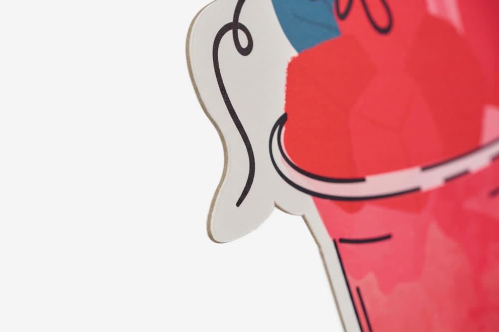 Close-up of a die-cut illustrated figure with red, pink, and blue graphic print on wood.