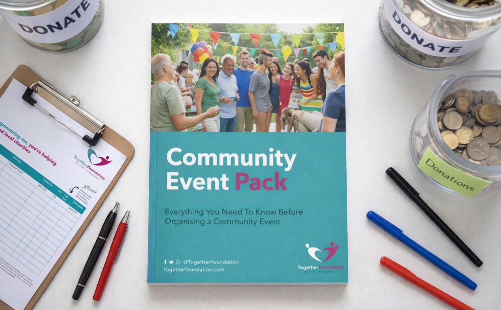 Booklet titled "Community Event Pack" on a table with donation jars, pens, and a clipboard.