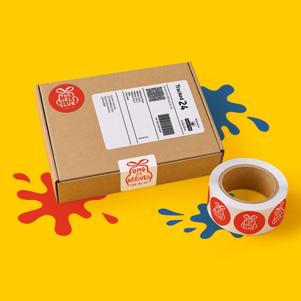 Brown shipping box and sticker roll on a yellow surface with red and blue paint splatters.