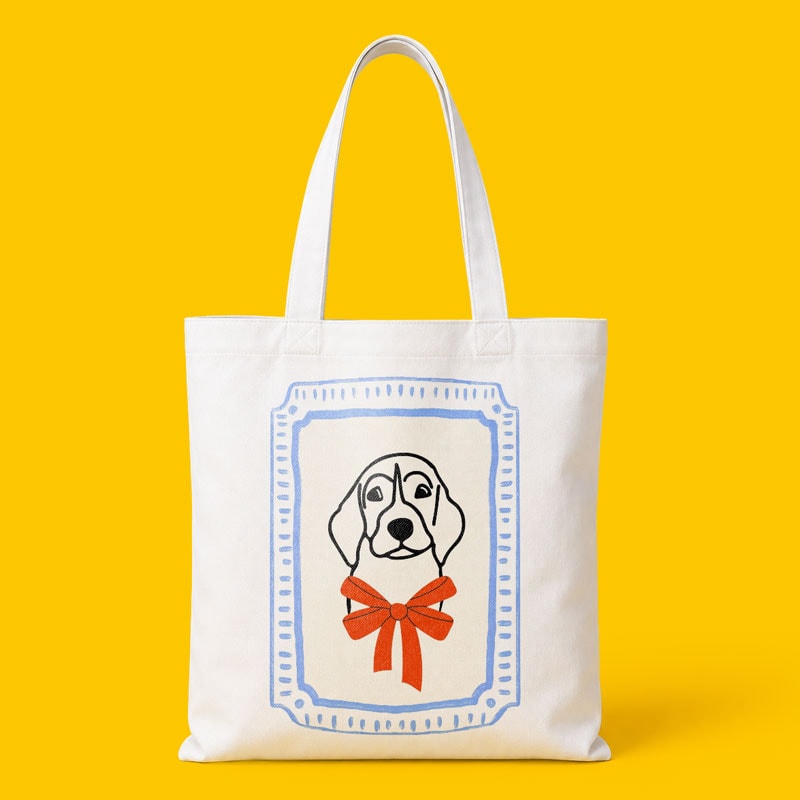 White tote bag with a dog illustration framed in blue and a red bow on a yellow background.