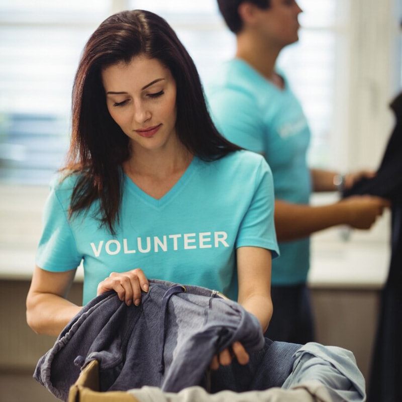 Woman wearing a volunteer shirt sorting clothes with another volunteer in the background.