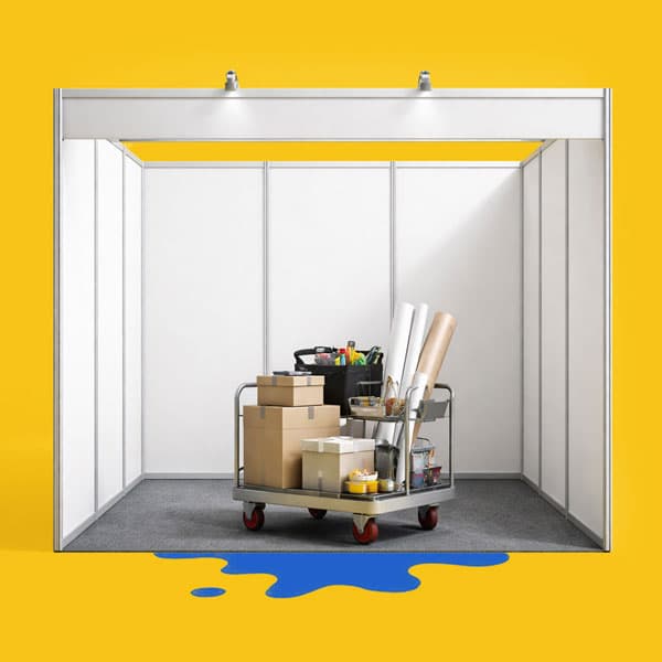 Empty booth with a cart full of boxes, tools, and rolled posters on a yellow background.