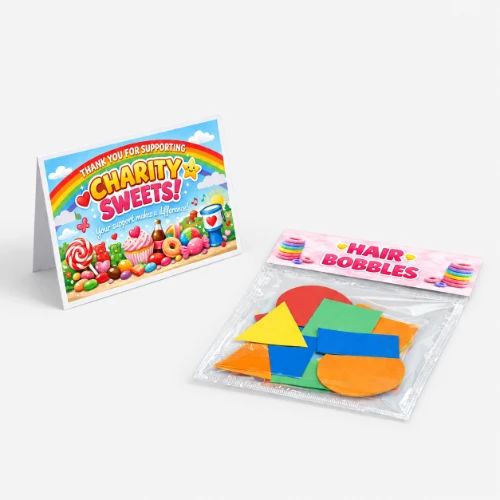 A charity sweets card bag topper and a pack of assorted colourful hair bobbles on a light surface.