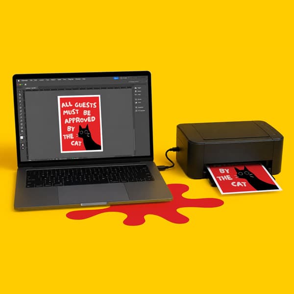 A laptop and printer on a yellow surface print a red sign featuring a black cat and white text.