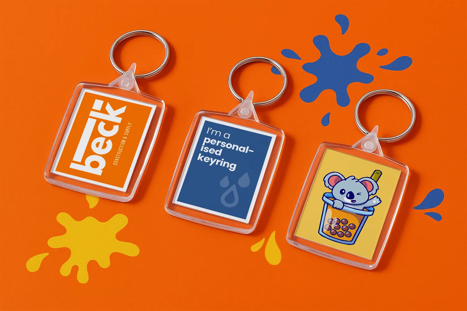Three rectangular keyrings with different designs on an orange surface with paint splatters.