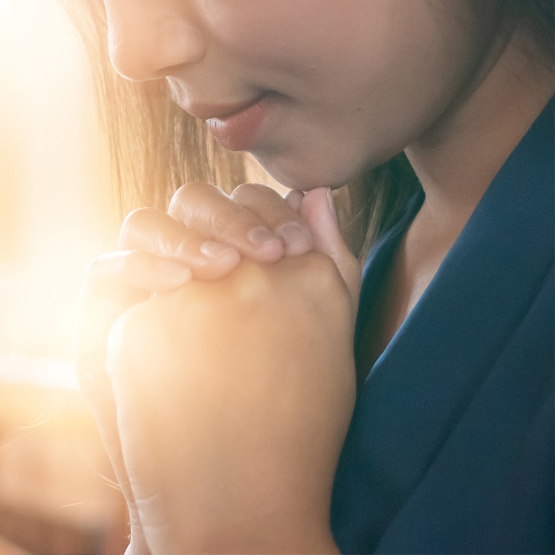 Close-up of a person with clasped hands, appearing thoughtful or in prayer, with soft lighting.