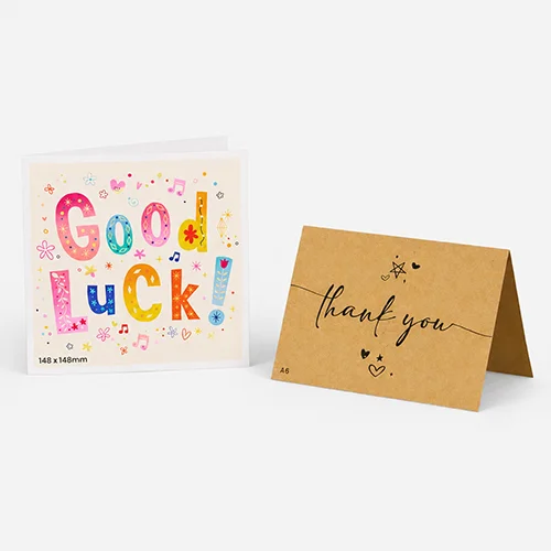 A "Good Luck!" printed greetings card and a "thank you" printed greetings card are standing side by side on a gray surface.