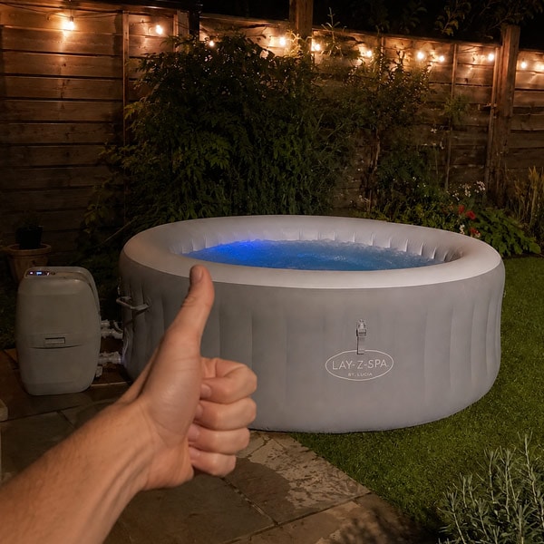 A hand gives a thumbs up in front of an inflatable hot tub in a backyard at night.