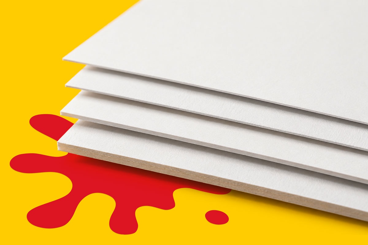 Four stacked white boards on a yellow surface with a red paint splatter underneath.