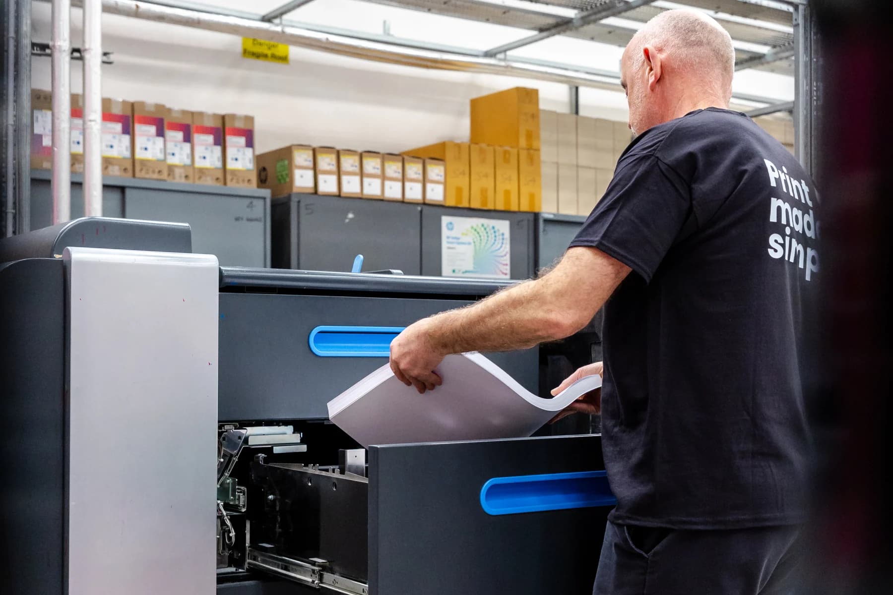 A man utilises a printer within a warehouse setting, surrounded by storage shelves and various supplies