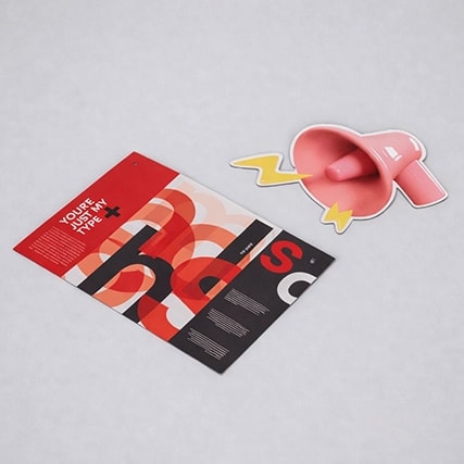 A colorful brochure and a pink megaphone-shaped sticker on a light gray surface.