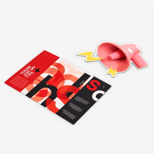 A colourful brochure and a pink megaphone-shaped sticker on a light gray surface.