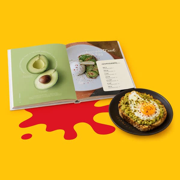 Open cookbook with avocado toast recipe beside a plate of toast with avocado and a fried egg.