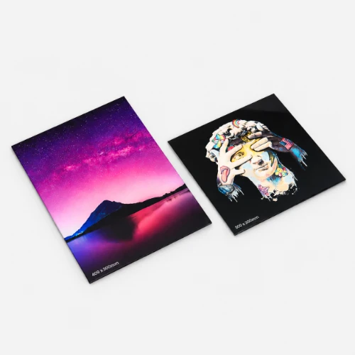 Two acrylic art prints on a grey surface: a mountain at sunset and a colourful abstract portrait.