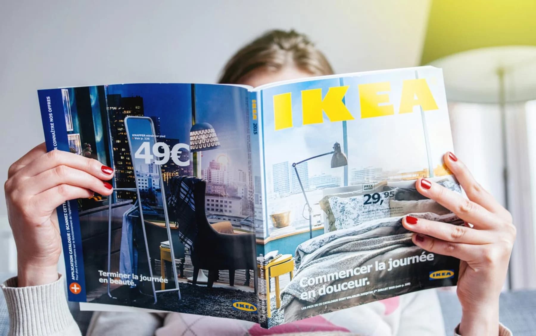A woman engrossed in reading a magazine featuring the IKEA logo prominently displayed on the cover