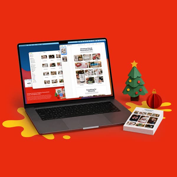 Laptop displaying photo gallery, next to printed photos, a mini Christmas tree, and ornament.