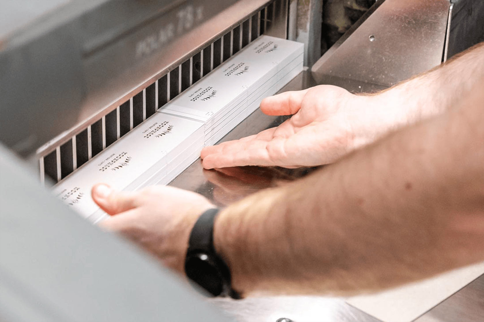 Person aligning a stack of printed cards in a paper cutting machine.