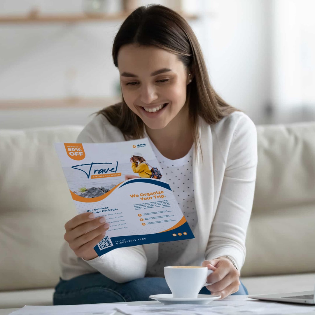 A woman is seated on a couch, holding a flyer, appearing focused and interested in the information presented.