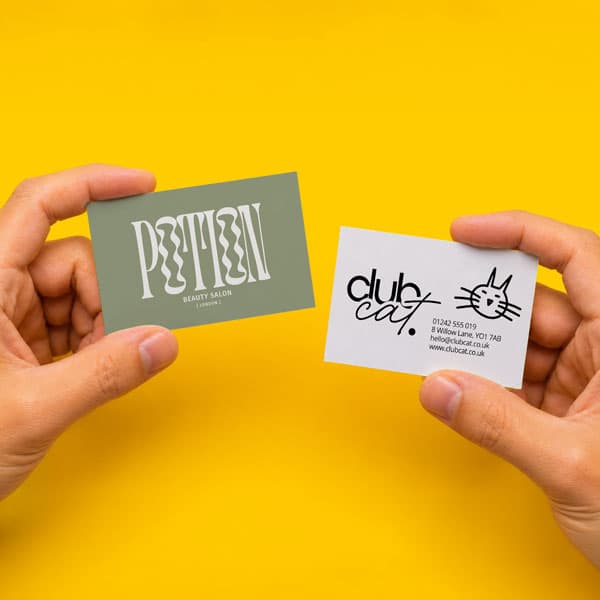 Two hands hold business cards for a beauty salon and a cat club against a yellow background.
