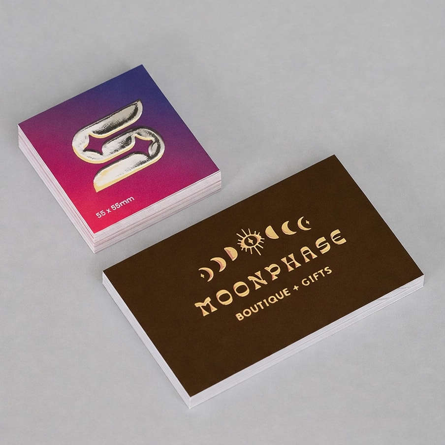 Two stacks of business cards, one with a silver metallic foil icon, one with gold foil "Moonphase Boutique + Gifts.