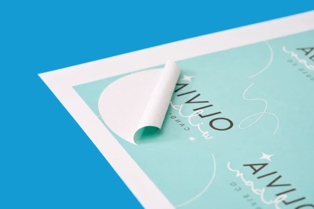 A close-up of a teal sticker sheet, with one corner peeled back, on a blue background.