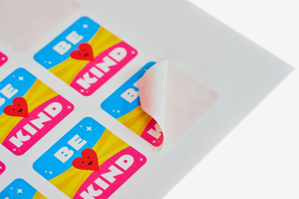 A sheet of colourful "Be Kind" stickers with one partially peeled off.