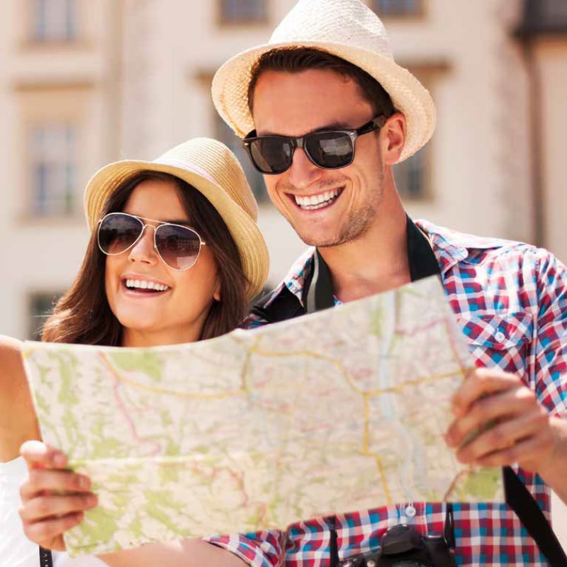 Two people wearing sunglasses and hats smiling while looking at a map outdoors.